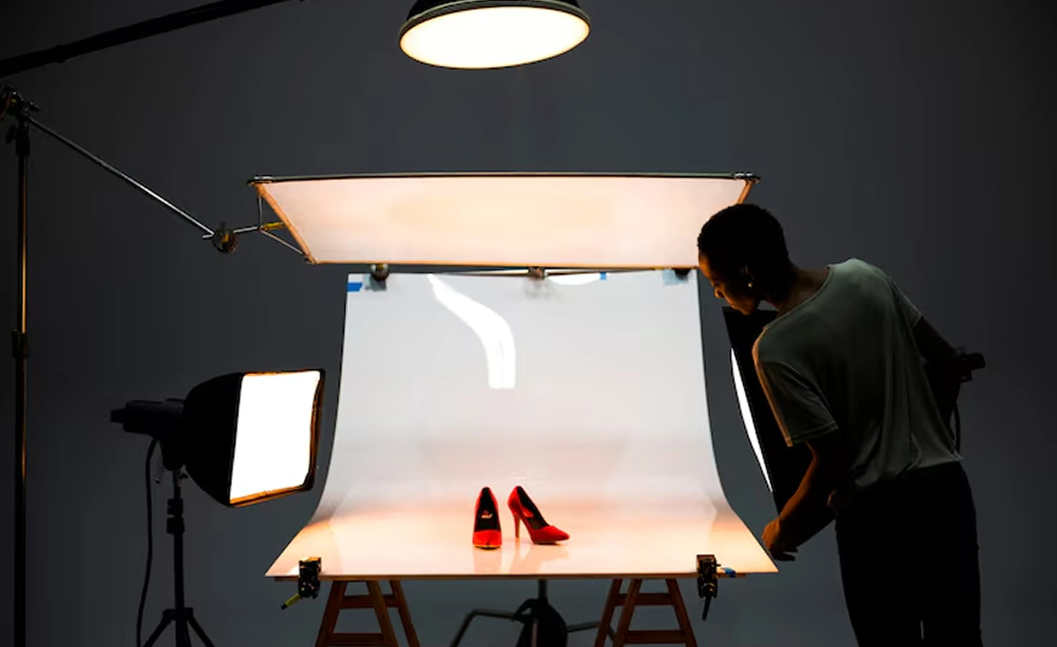 A product photographer lighting a pair of red heels in a studio